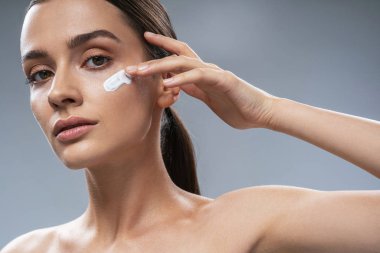 Gri arka planda yüz bakımı yapan konsantre bir kız.