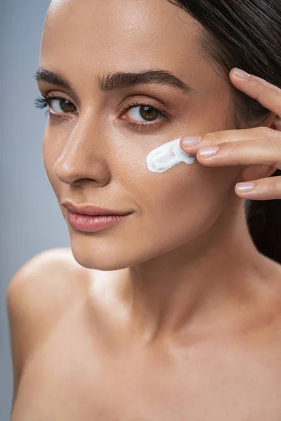 Menina bonita cuidando da pele facial contra fundo cinza — Fotografia de Stock