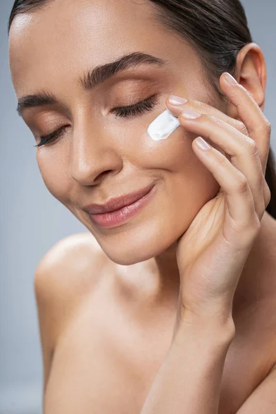 Pretty girl taking care of facial skin against grey background — Stock Photo, Image
