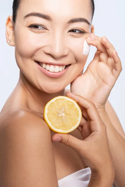 Mujer joven y feliz aplicando crema en la piel facial — Foto de Stock