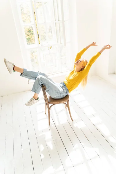 リラックスした若いです女性で黄色のセーターに座っている上の椅子の近くに窓 — ストック写真