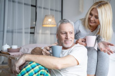 Elinde çayla gülümseyen kadın stok fotoğrafına bakıyor.