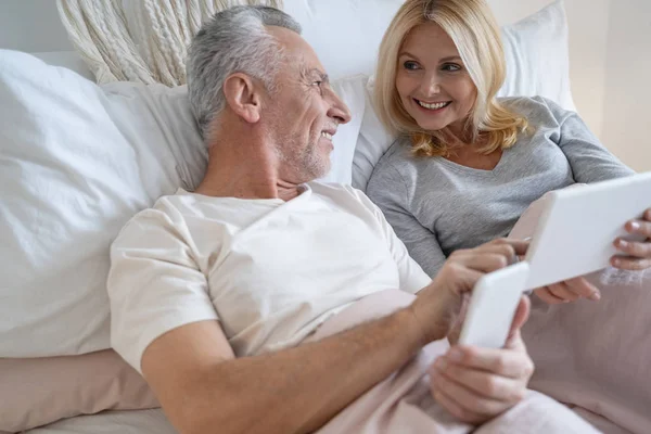 Starší pár s gadgets doma usměvavý stock fotografie — Stock fotografie