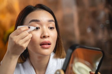 Asyalı kız içeride göz damlası kullanıyor.