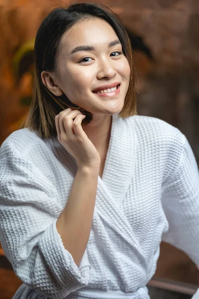Mujer asiática sonriente con albornoz blanco en salón de belleza —  Fotos de Stock