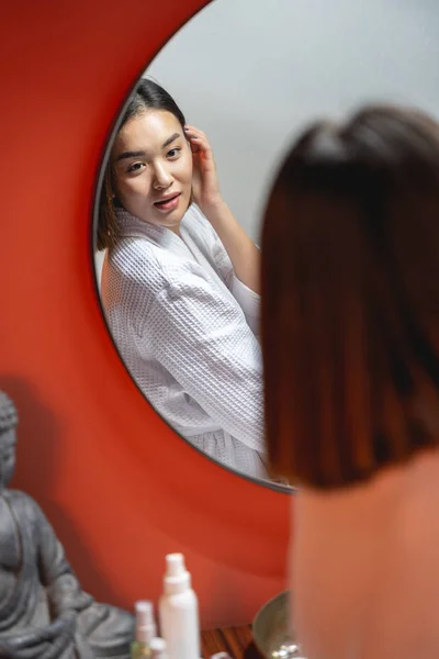 Молодая красивая азиатка смотрит в зеркало в помещении — стоковое фото