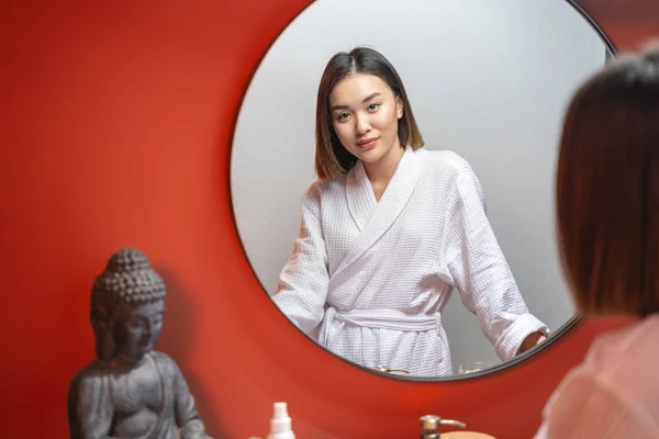 Спокойная азиатка смотрит в зеркало в помещении — стоковое фото