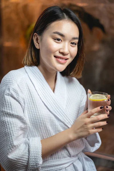 Милая улыбающаяся азиатка пьет чай после косметических процедур в салоне — стоковое фото