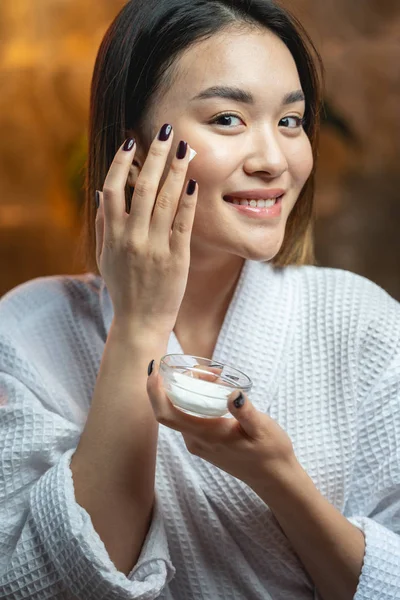 Linda chica asiática aplicando crema en su piel —  Fotos de Stock