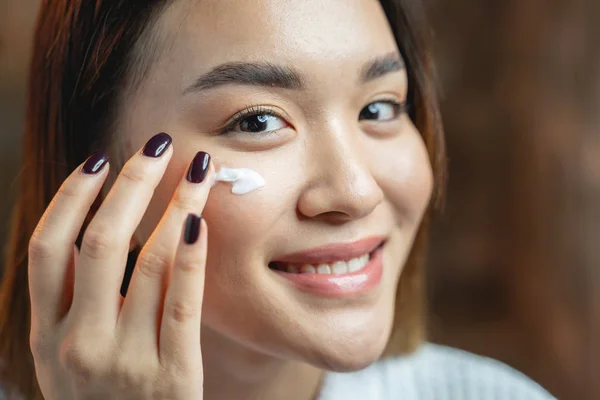 Bastante agradable chica asiática aplicando crema en su piel — Foto de Stock