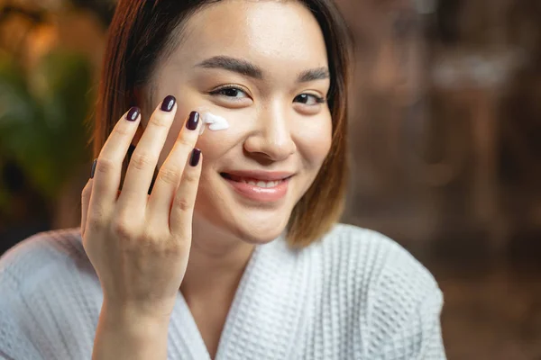 Atractiva chica asiática aplicando crema en su piel —  Fotos de Stock