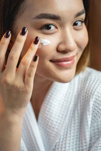 Hermosa chica asiática aplicando crema en su piel — Foto de Stock