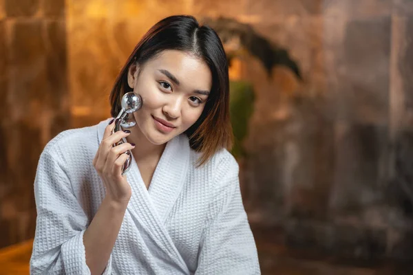 Asyalı güzel kadın yüz geliştirme için modern masaj aletleri kullanıyor. — Stok fotoğraf