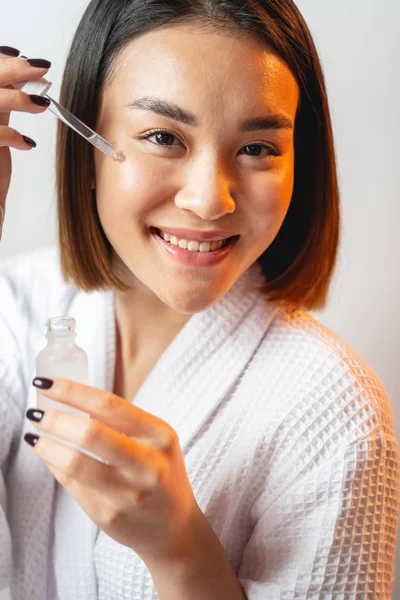 Csinos ázsiai nő alkalmazása kozmetikai folyadék az arcán — Stock Fotó