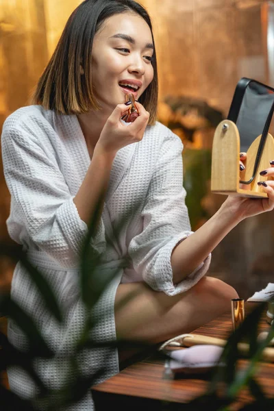 Asiática linda dama en blanco albornoz poniendo maquillaje en el interior — Foto de Stock