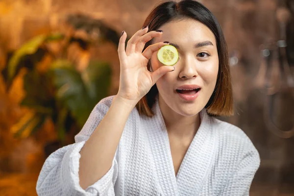 Sorrindo menina asiática posando para câmera com fatias de pepino — Fotografia de Stock