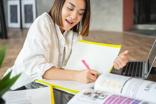Asiatische lächelnde junge Frau arbeitet mit Papieren und Laptop — Stockfoto