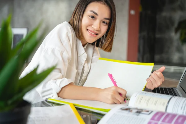 Asiatische fröhliche junge Frau arbeitet mit Papieren und Laptop — Stockfoto