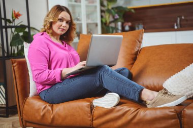 Cute female person sitting with computer on sofa