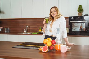Positive delighted plump girl drinking green smoothie