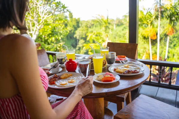 Jovem mulher comendo ovos fritos com bacon e frutas — Fotografia de Stock