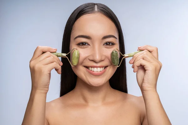 Sorridente belle guance femminili massaggianti con rullo viso — Foto Stock