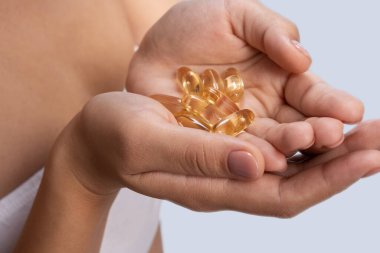 Omega 3 balık yağı kapsüllerini elinde gösteren bir kadın.