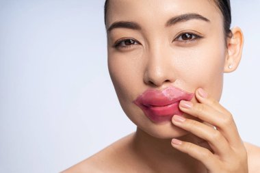 Smiling Asian lady is putting patch on lips clipart