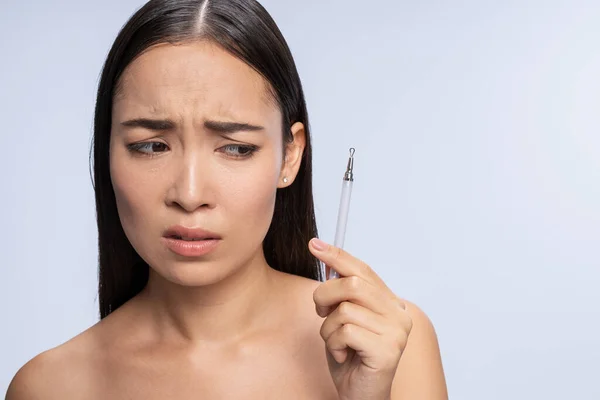 Scared woman looking at comedone extractor in studio — Stock Photo, Image