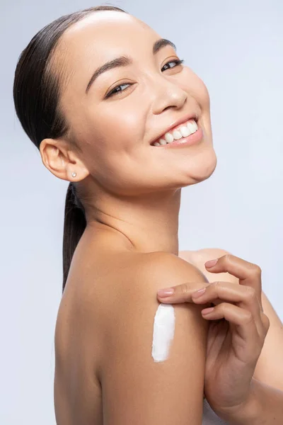 Happy Asian lady rubbing lotion into the skin — Stock Photo, Image