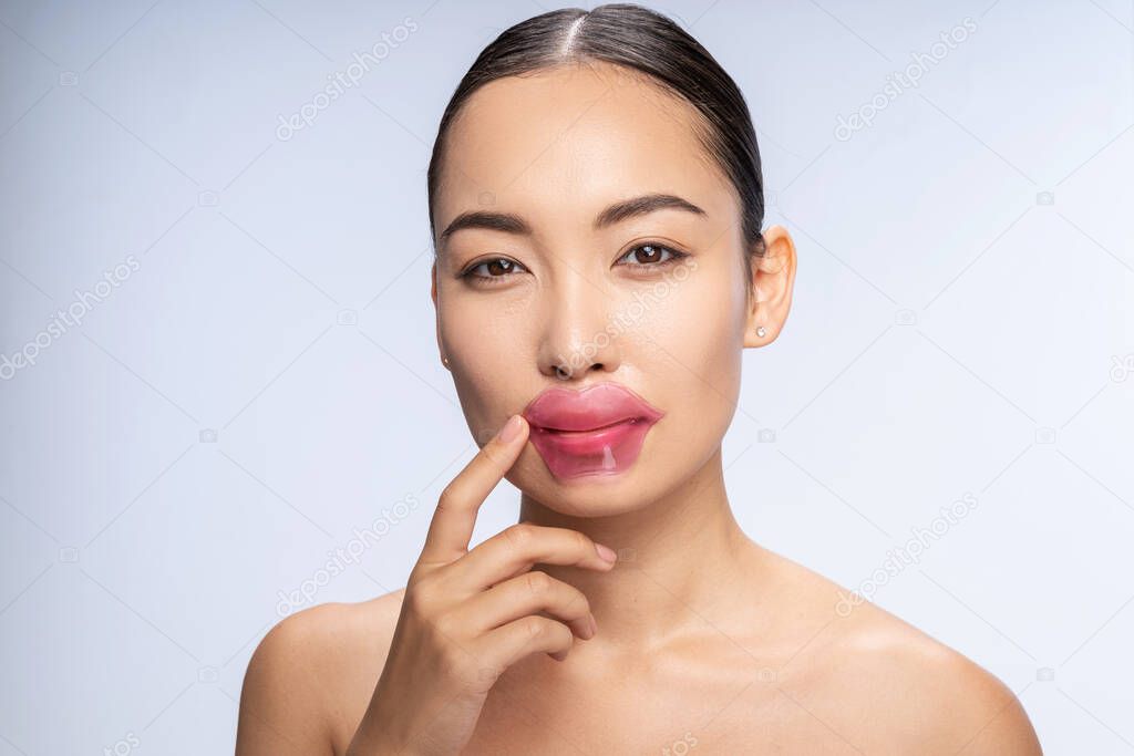 Smiling Asian woman is putting lip patches
