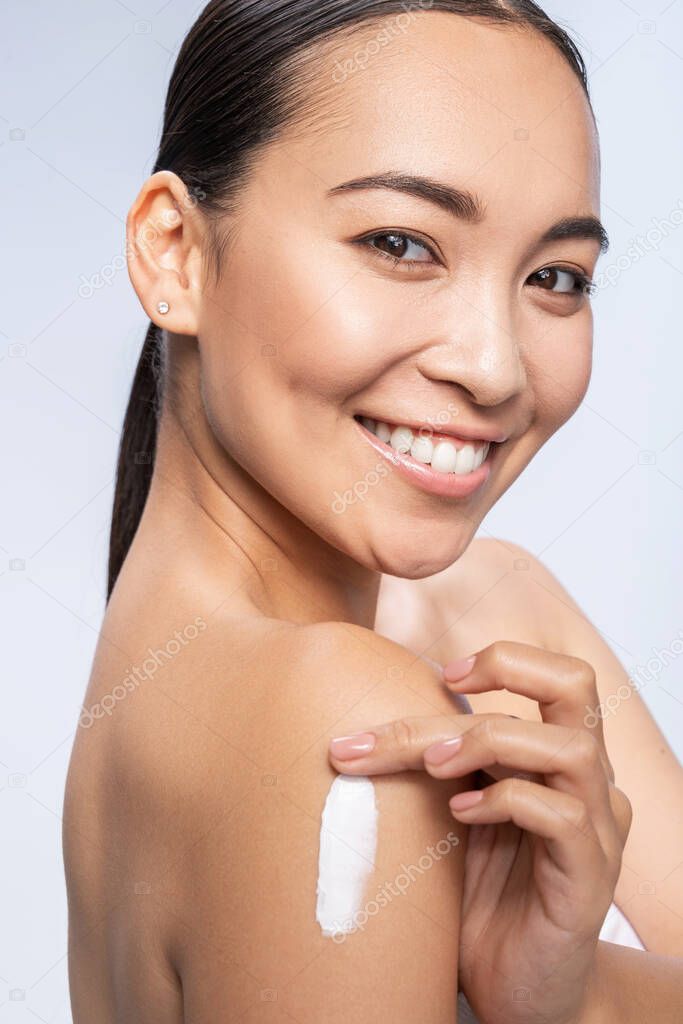 Happy pretty female applying lotion on hand
