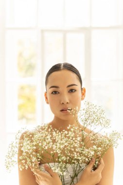 Beyaz bluzlu güzel Asyalı kadın pencerenin yanında oturuyor.