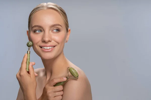 Vrolijke jonge vrouw doet gezichtsmassage met jade roller — Stockfoto