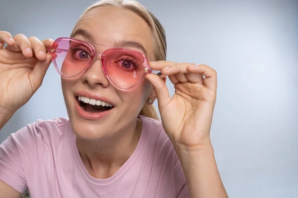 Fröhliches blondes Mädchen demonstriert ihre rosa Brille — Stockfoto