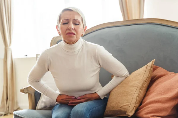 Senhora envelhecida contorcendo-se em uma dor abdominal — Fotografia de Stock