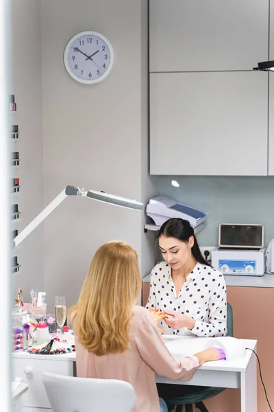 Kind young manicure master polishing nails for client — Stock Photo, Image