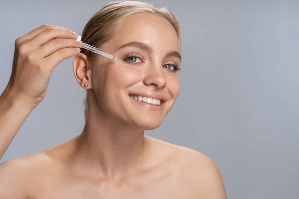 Positivo felice giovane femmina mettendo siero sul viso — Foto Stock