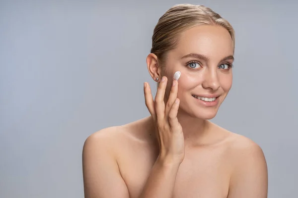 Mujer rubia encantada positiva usando crema nueva — Foto de Stock