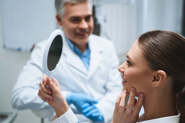 Happy woman looking into mirror in dental clinic stock photo — Stock Photo, Image