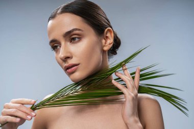 Bitki yaprağı olan sakin, genç ve çekici bir kadın.