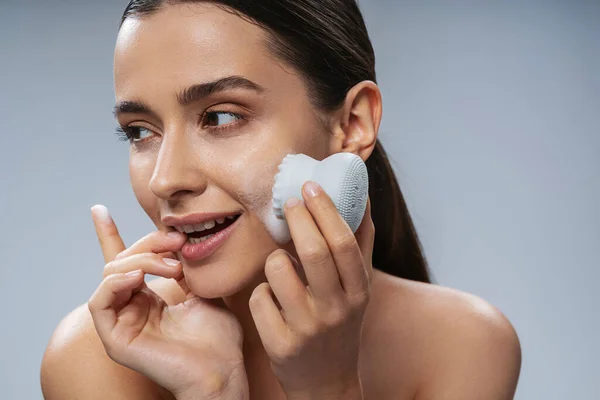 Joven alegre haciendo limpieza facial con dispositivo de cosméticos — Foto de Stock