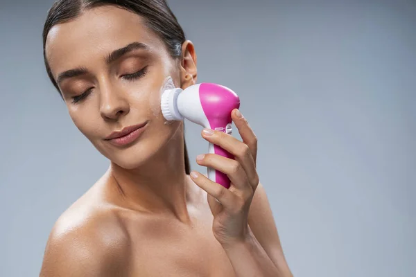 Mujer joven haciendo facial con cepillo digital — Foto de Stock