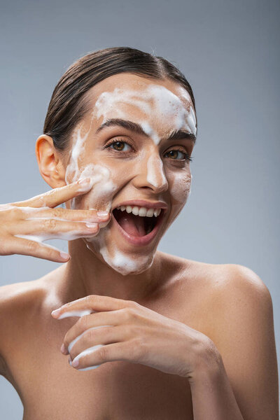 Веселая женщина веселится во время очищения лица
