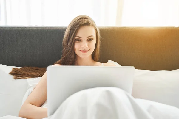 Chica alegre sentado con un ordenador portátil en la cama — Foto de Stock