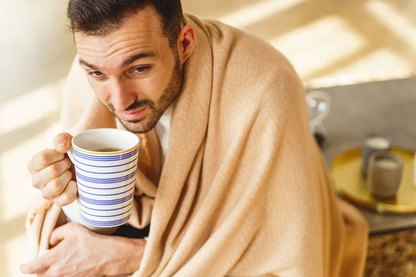Sick man wrapped in a plaid sitting at home — Stock Photo, Image