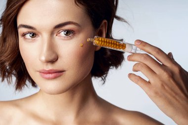 Güzel genç bir kadın yüzüne krem sürüyor.