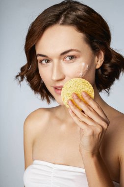 Mutlu genç kadın, yüz temizleme tedavisi uyguluyor.