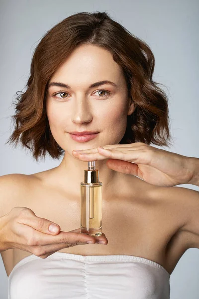 Vidám fiatal hölgy gazdaság kozmetikai olaj a bőr — Stock Fotó