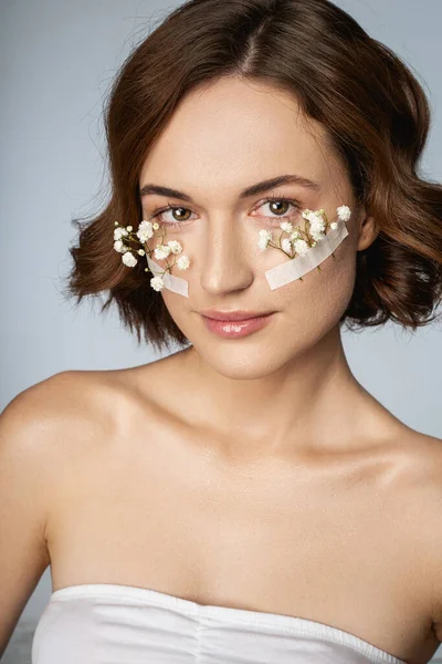 Glimlachende jonge vrouw met kleine witte bloemen op gezicht — Stockfoto